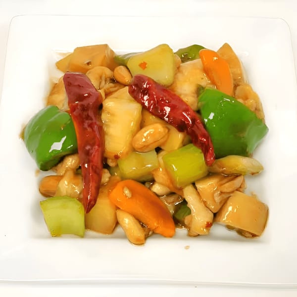 Kung Pao Chicken with red chilies, green and orange bell peppers, and peanuts on a white plate.